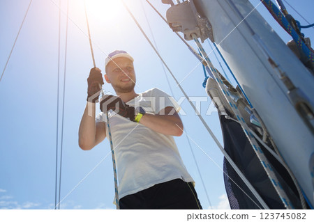 Male captain on deck of sailboat opening sails pulling the rope Male captain on deck of sailboat opening sails pulling the rope 123745082