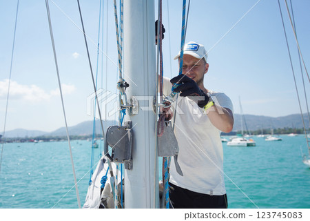 Male captain on deck of sailboat opening sails pulling the rope 123745083