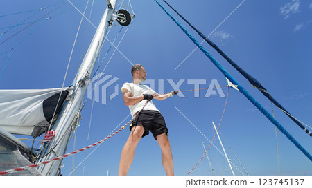 Male captain on deck of sailboat opening sails pulling the rope Male captain on deck of sailboat opening sails pulling the rope 123745137
