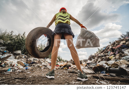 Woman volunteer helps clean the field of plastic garbage and old tires. Woman volunteer helps clean the field of plastic garbage and old tires. 123745147