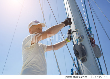 Male captain on deck of sailboat opening sails pulling the rope 123745158