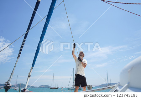 Male captain on deck of sailboat opening sails pulling the rope Male captain on deck of sailboat opening sails pulling the rope 123745183