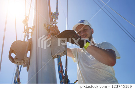 Male captain on deck of sailboat opening sails pulling the rope 123745199