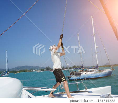 Male captain on deck of sailboat opening sails pulling the rope 123745228