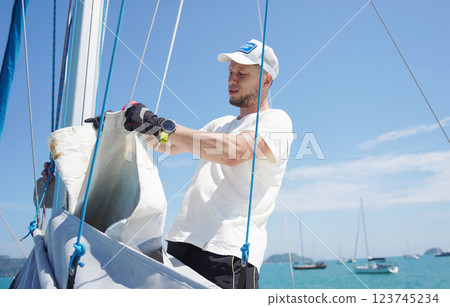 Male captain on deck of sailboat unpacking sails pulling zipper Male captain on deck of sailboat unpacking sails pulling zipper 123745234