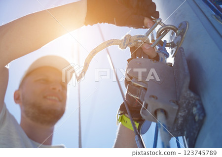 Male captain on deck of sailboat opening sails pulling the rope Male captain on deck of sailboat opening sails pulling the rope 123745789