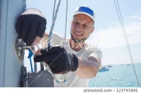 Male captain on deck of sailboat opening sails pulling the rope Male captain on deck of sailboat opening sails pulling the rope 123745806