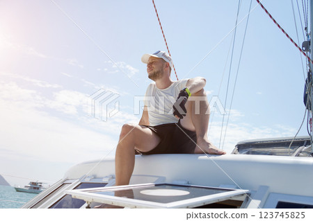 A man is calmly sitting on the deck of a beautiful sailboat A man is calmly sitting on the deck of a beautiful sailboat 123745825