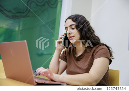A woman talking on the phone while using a computer A woman talking on the phone while using a computer 123745834