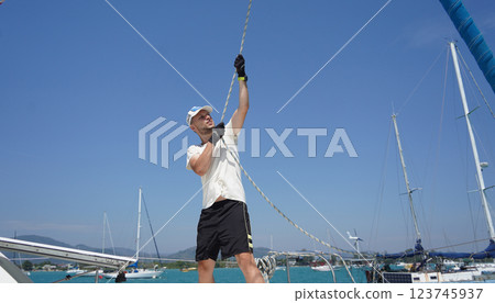 Male captain on deck of sailboat opening sails pulling the rope Male captain on deck of sailboat opening sails pulling the rope 123745937