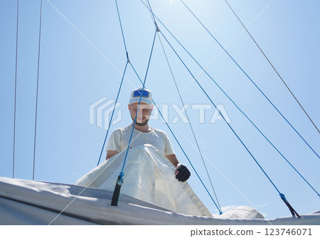 Male captain on deck of sailboat unpacking sails pulling zipper Male captain on deck of sailboat unpacking sails pulling zipper 123746071