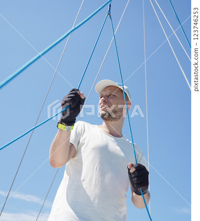 Male captain on deck of sailboat opening sails pulling the rope Male captain on deck of sailboat opening sails pulling the rope 123746253