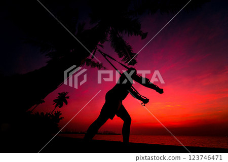 The athlete performs exercises on the beach with fitness straps 123746471