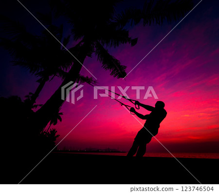 The athlete performs exercises on the beach with fitness straps 123746504