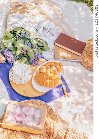 Cozy Outdoor Picnic with Croissants and Lilac Flowers charming picnic setup with croissants, tea, lilac flowers, books, and pastries on a blanket under dappled sunlight in spring day Cozy Outdoor Picnic with Croissants and Lilac Flowers charming picnic setup with croissants, tea, lilac flowers, books, and pastries on a blanket under dappled sunlight in spring day 123746805