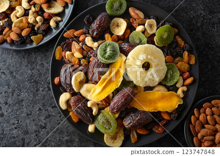 Dried tropical fruits, nuts, and raisins in black plate. 123747848