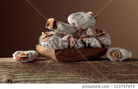 Dried persimmons in a wooden dish on a brown background. 123747854