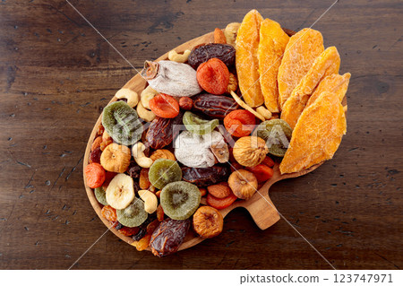 Dried mango slices, tropical fruits, nuts, and raisins on an old wooden table. Dried mango slices, tropical fruits, nuts, and raisins on an old wooden table. 123747971