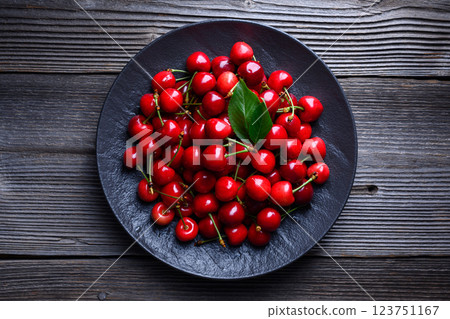 Top view of black plate with ripe cherries on a rustic wooden table 123751167