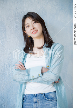 身著休閒服飾的女子麵帶微笑，仰望淺藍色背景，雙臂交叉，看著鏡頭 123751477