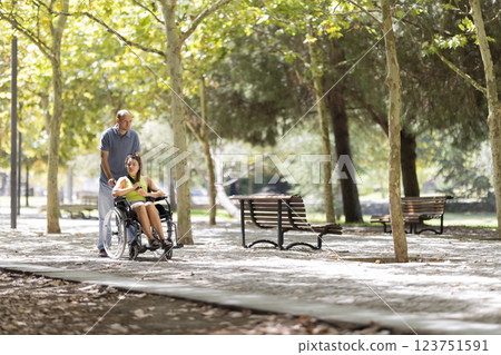 Nurse pushing patient in wheelchair through sunny park path 123751591