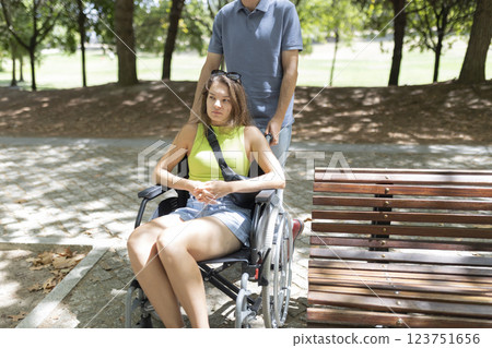 Man pushing sad disabled woman in wheelchair in park 123751656