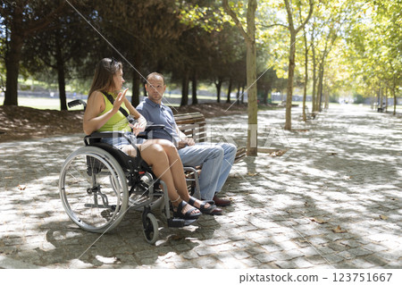 Young woman in wheelchair talking with friend in park 123751667