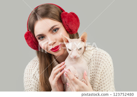 Beautiful woman wearing red fluffy ear muffs hugging hairless cat pet Beautiful woman wearing red fluffy ear muffs hugging hairless cat pet 123752480