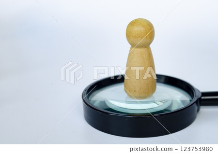 A wooden doll standing on magnifying glass. Representing the chosen one or leadership concept. A wooden doll standing on magnifying glass. Representing the chosen one or leadership concept. 123753980