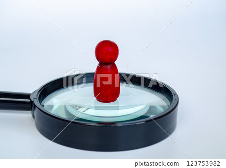 A red wooden doll standing on magnifying glass. Representing the chosen one or leadership concept 123753982