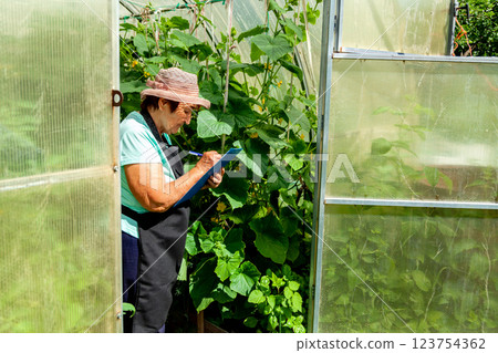 Elderly Female Farmer Observing Plants and Taking Notes Elderly Female Farmer Observing Plants and Taking Notes 123754362