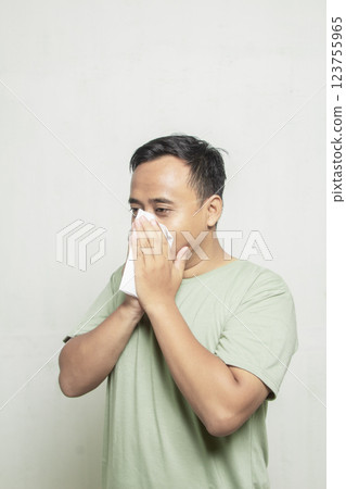 Asian man with glasses sneezing with tissue in his nose isolated on white background 123755965