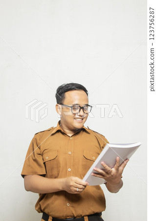 Indonesian male teacher in khaki uniform invites people to read books, the man is shown with part of his body on a white background 123756287