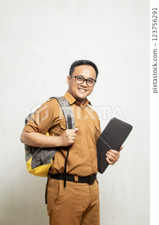 Profile of Indonesian school teacher in khaki clothes standing proudly while carrying a big bag and black laptop on his chest, concept of teacher going to school to teach Profile of Indonesian school teacher in khaki clothes standing proudly while carrying a big bag and black laptop on his chest, concept of teacher going to school to teach 123756291