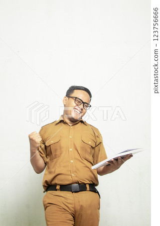 Indonesian Middle School Teacher is excited. The teacher is wearing old khaki and carrying a book Indonesian Middle School Teacher is excited. The teacher is wearing old khaki and carrying a book 123756666