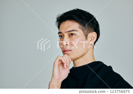 A young man in his twenties thinking with his chin in his hand A young man in his twenties thinking with his chin in his hand 123756875
