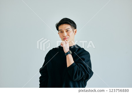 A young man in his twenties thinking with his chin in his hand 123756880