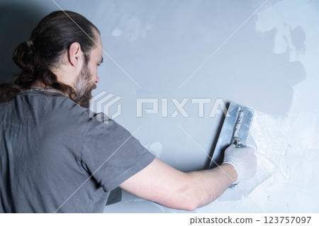 A craftsman uses a trowel to apply epoxy adhesive for surface repair in a bright room. 123757097