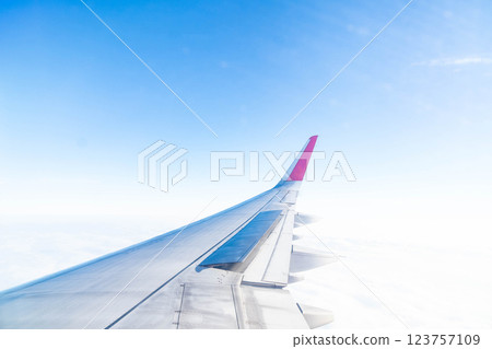 Gazing out from the cabin, a vivid view reveals the graceful curve of an aircraft wing. Lush clouds stretch endlessly below, capturing the essence of flight, adventure, and boundless freedom. 123757109