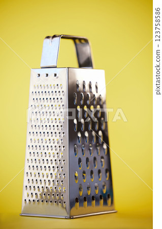 Metal or steel cheese grater for grocery cooking, food preparation and culinary help or support. Silver, metallic or home kitchenware appliance with cut pattern shredder isolated on yellow background Metal or steel cheese grater for grocery cooking, food preparation and culinary help or support. Silver, metallic or home kitchenware appliance with cut pattern shredder isolated on yellow background 123758586