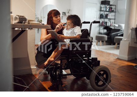 Hair, beauty and inclusive barber grooming child in a wheelchair, relax while digital tablet and comfort. Care, disability and child development with handicapped boy enjoying pamer treatment haircut 123759064