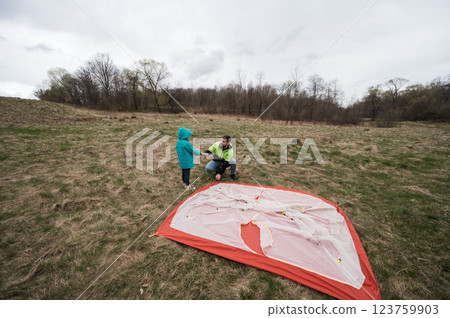 Enjoying a Family Day Outdoors as a Parent Teaches Their Child How to Set Up a Tent on a Cloudy Day in the Countryside 123759903