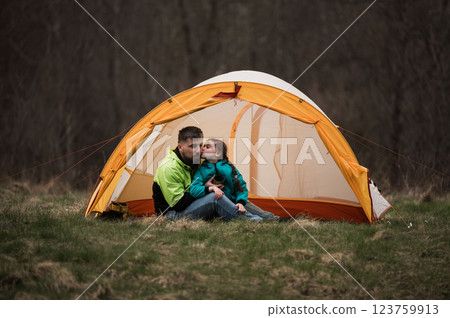 Couple enjoying a tender moment under a bright orange tent in a peaceful meadow during a serene evening outdoors 123759913
