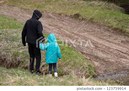 Two children exploring nature together by a stream in early spring, dressed in warm jackets, creating cherished memories amidst the lush greenery 123759914