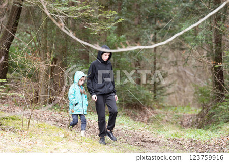 Siblings exploring a serene forest path during a cool afternoon, wrapped in cozy hooded jackets while nature unfolds its tranquility around them Siblings exploring a serene forest path during a cool afternoon, wrapped in cozy hooded jackets while nature unfolds its tranquility around them 123759916