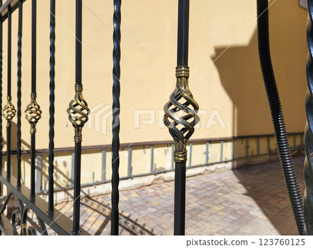 A fence with forged bronze elements on the background of a beige wall of the house 123760125