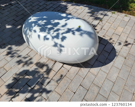 On a beautiful sunny day, a single white decorative concrete oval lies in a shady garden. 123760134