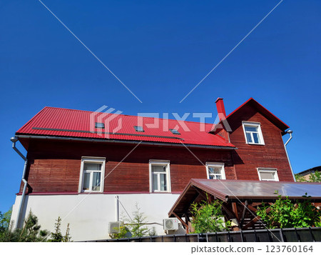 A brown house with a red roof against a blue sky background. 123760164