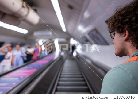 Budapest, Hungary, August 30, 2022. Shot of subway escalators. Close-up of a young man with curly hair and glasses, blurred background. Lifestyle using public transportation. 123760310
