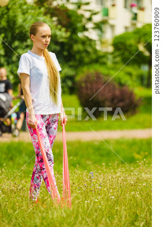 Girl doing exercises outdoor, using resistance fit band. 123760909